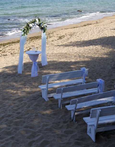 Romantic beach wedding setup with white floral arch and turquoise ocean